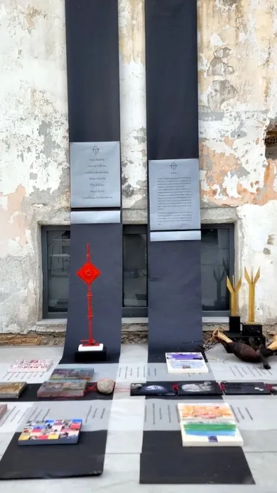 Άποψη από την εγκατάσταση «Διαδρομές»: χάρτινοι διάδρομοι σε μαύρο και γκρι στρωμένοι στο δάπεδο βιομηχανικού χώρου, με τα έργα των καλλιτεχνών και τυπωμένους στίχους τοποθετημένους πάνω τους.