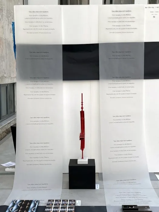 Άποψη από την εγκατάσταση «Διαδρομές»: χάρτινοι διάδρομοι σε μαύρο και γκρι στρωμένοι στο δάπεδο βιομηχανικού χώρου, με τα έργα των καλλιτεχνών και τυπωμένους στίχους τοποθετημένους πάνω τους.