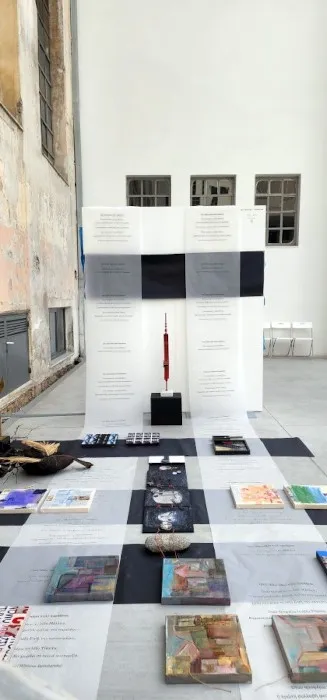 Άποψη από την εγκατάσταση «Διαδρομές»: χάρτινοι διάδρομοι σε μαύρο και γκρι στρωμένοι στο δάπεδο βιομηχανικού χώρου, με τα έργα των καλλιτεχνών και τυπωμένους στίχους τοποθετημένους πάνω τους.